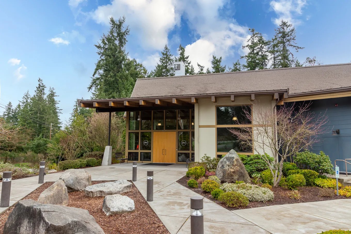 Exterior of Island Church on Bainbridge Island, a single-story modern building with a deep timber eave, glass entry and stone landscaping set against Pacific Northwest evergreens